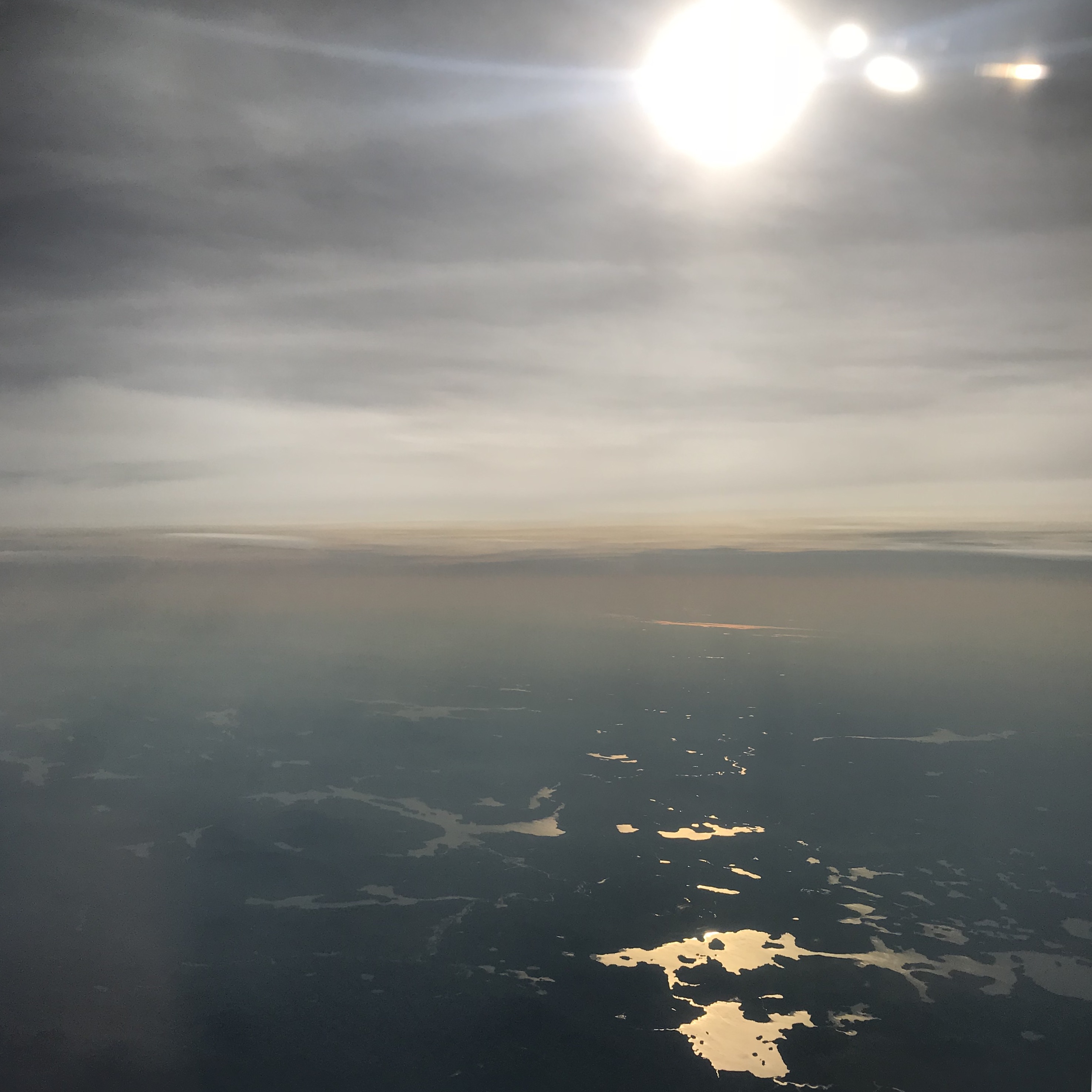 Earth seen from an airplane close to sunset, with the sun reflecting in lakes