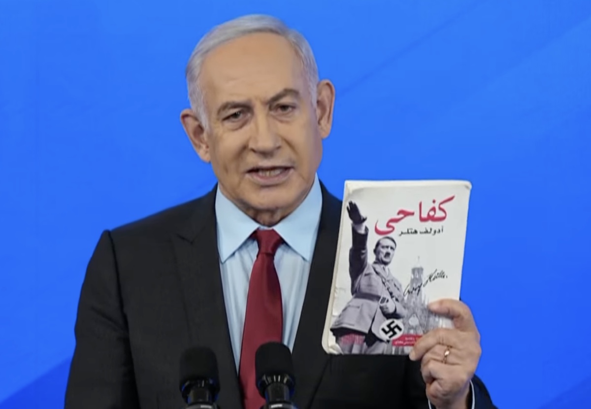 Netanyahu standing at a lectern and holding up an Arabic copy of Hitler’s
          Mein Kampf during a press conference