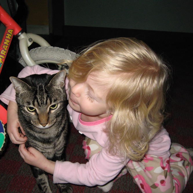 A very young, blond girl in her pyjamas sits on the floor next to Esteban,
             gingerly hugging him